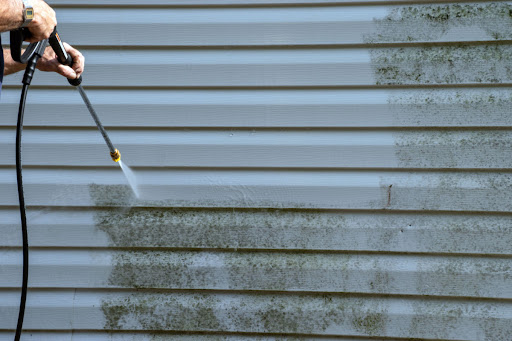 An unknown person is power washing vinyl siding which is stained by mildew.