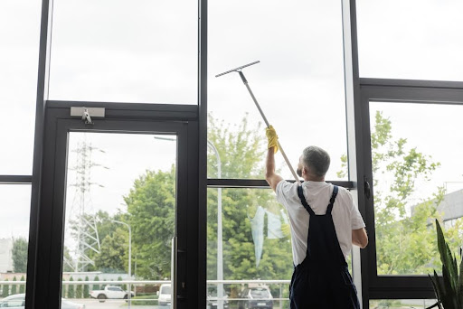 back view of man in overalls washing large office windows with window squeegee